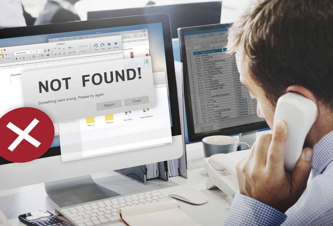 Geschäftsmann telefoniert an seinem Schreibtisch, auf dem Monitor erscheint die Fehlermeldung: Not Found!